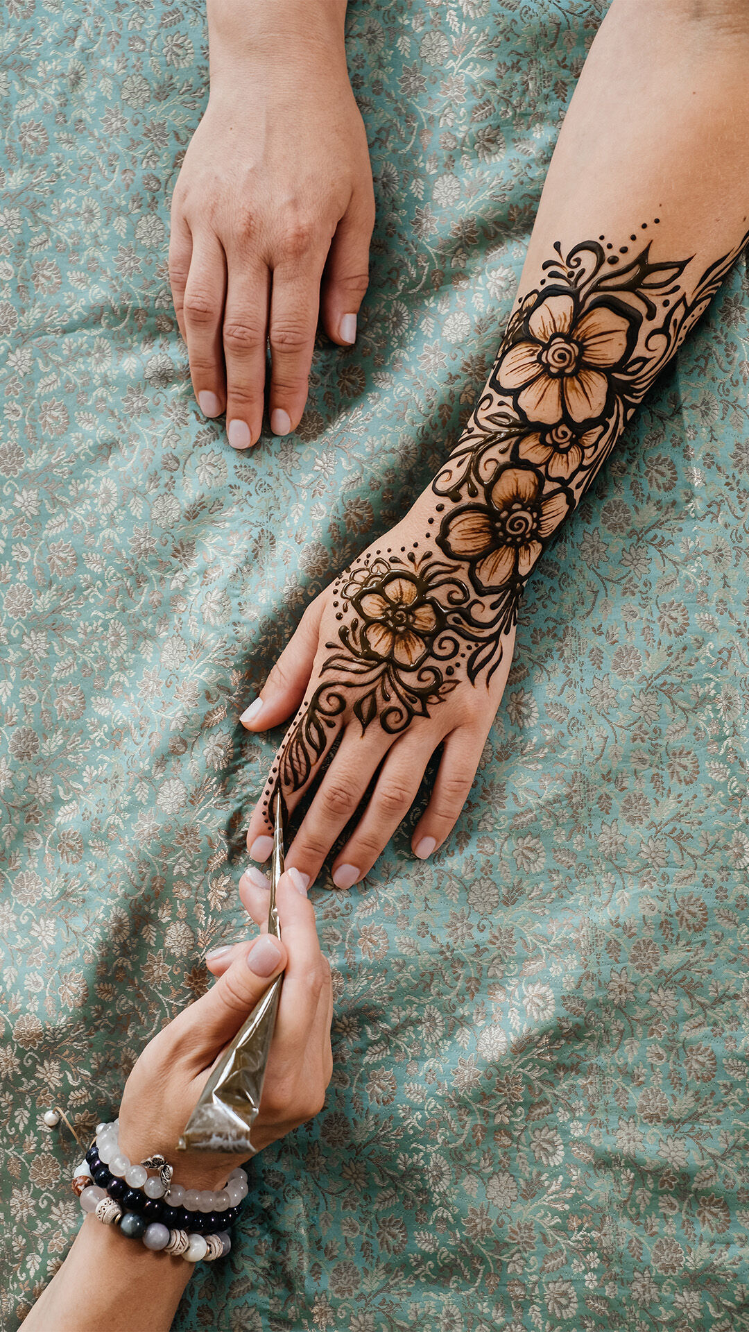 Close-up of an artist applying intricate bridal mehendi on a person's arm, featuring detailed traditional patterns.